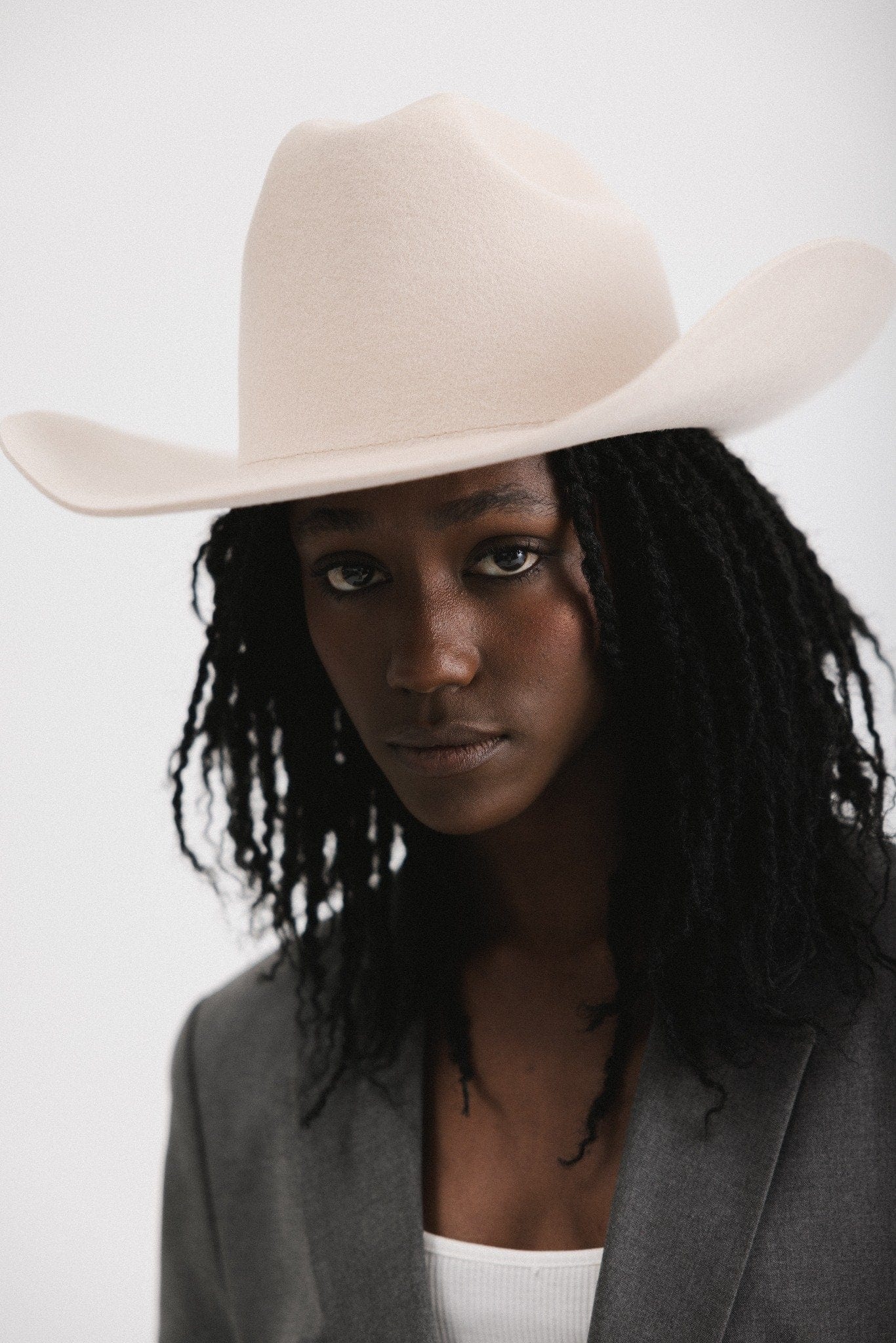 Woman wearing a cream cowboy hat and grey blazer against a white background #color_cream