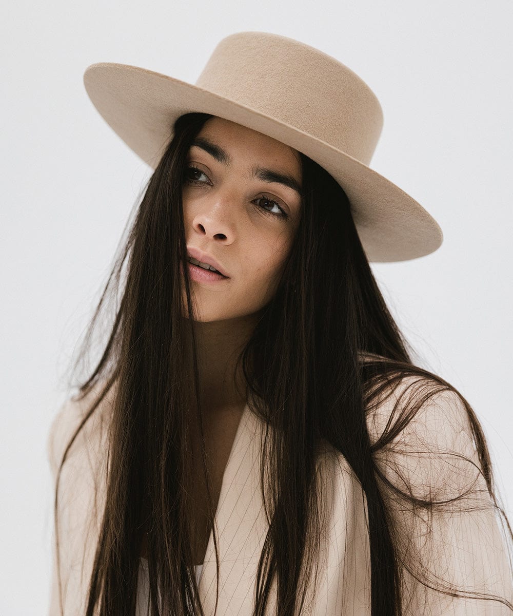Woman with long hair wearing a tan boater-style hat and a cream blazer against a plain background #color_tan