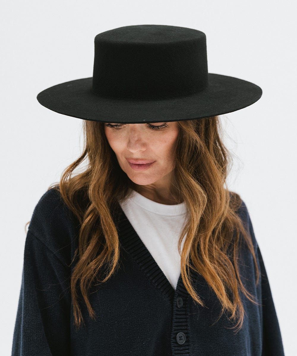 Woman wearing a black boater-style hat and a dark blue shirt against a plain background #color_black