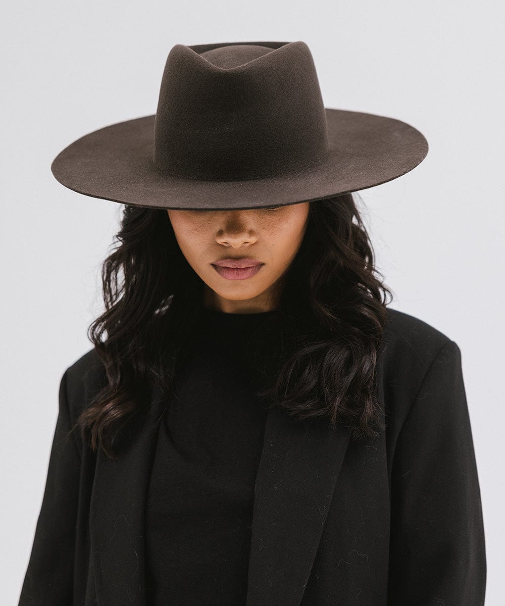 Woman wearing a dark brown wide brim felt hat with a triangle crown and a black blazer against a white background #color_dark brown