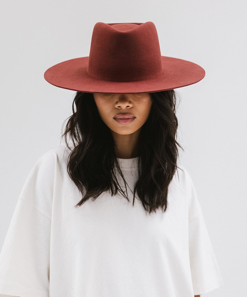 Woman wearing a rusty red wide brim felt hat with a triangle crown and a white shirt against a white background #color_rusty red