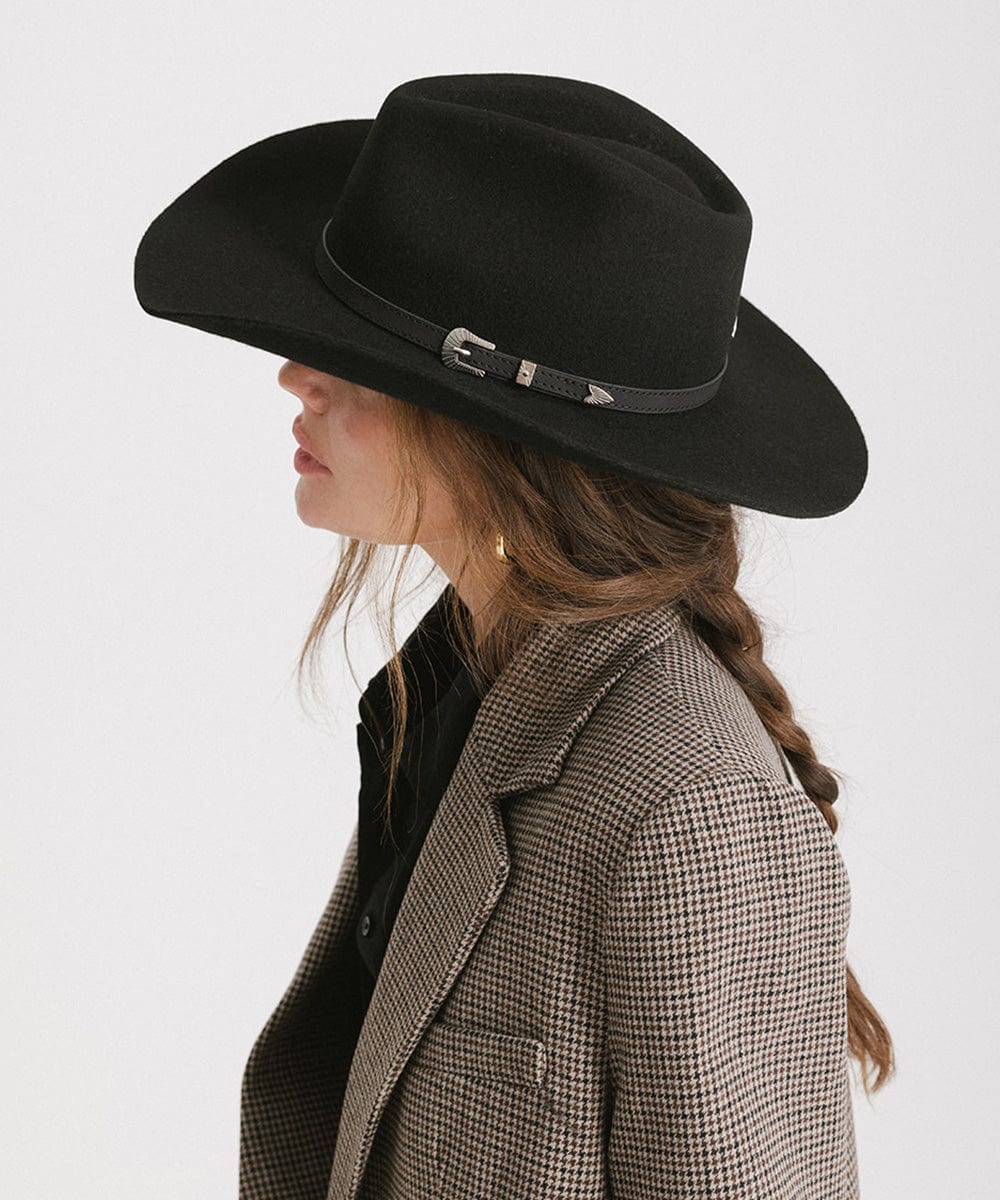 Woman wearing a black cowboy hat with an attached leather band and a blazer against a white background  #color_black