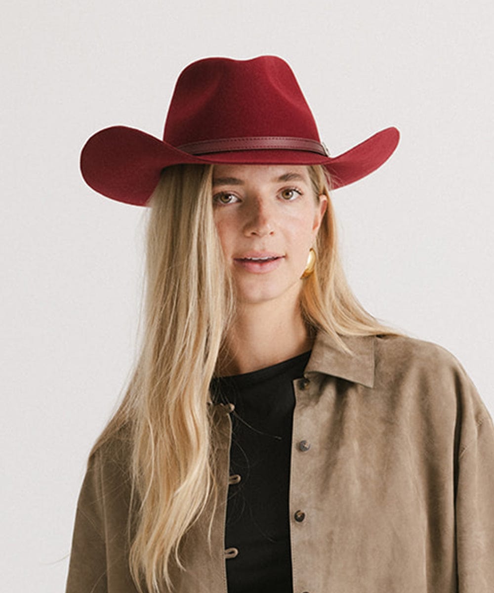 Woman wearing a burgundy cowboy hat with an attached leather band and a beige shirt against a white background #color_burgundy