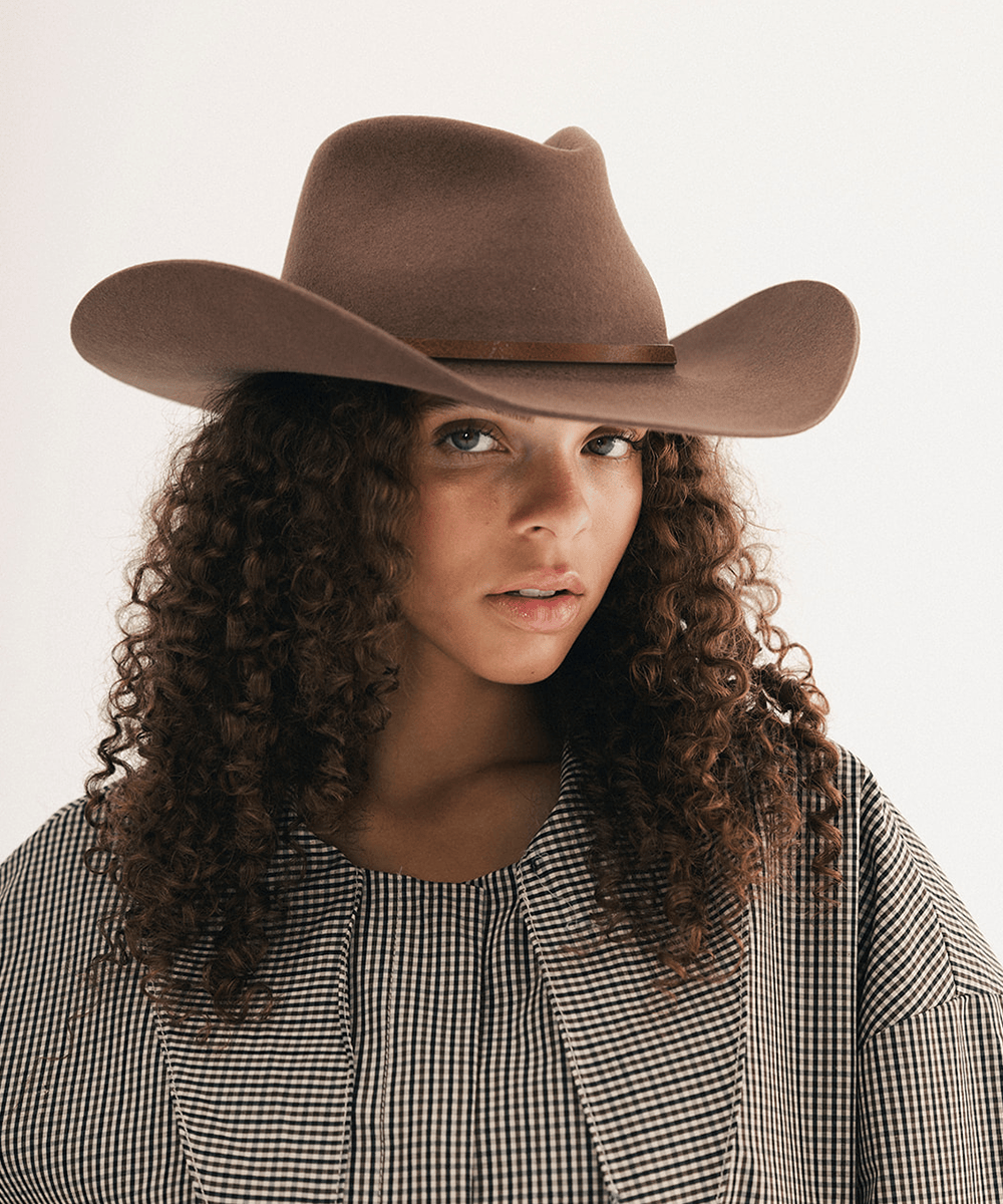 Woman wearing a brown cowboy hat with a brown hat band and a plaid shirt #color_chocolate