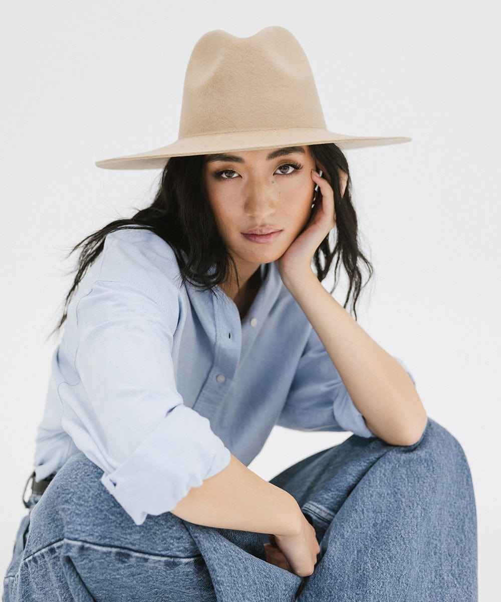 Woman wearing a tan wide brim hat, a blue shirt, and blue jeans against a plain background #color_tan