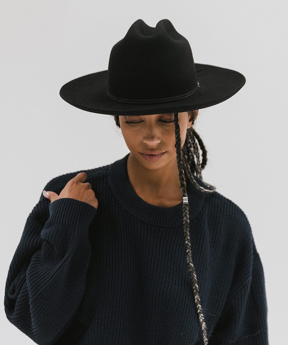 Woman wearing a black Western hat with a classic cattleman crown and a black hat band, and a dark blue sweatshirt against a plain background  #color_black