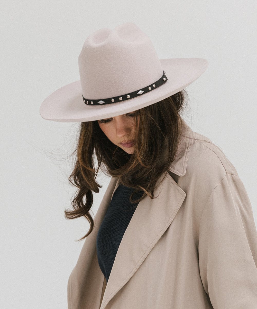 Woman wearing an ivory colored Western hat with a classic cattleman crown and black hat band, and a beige coat against a plain background #color_ivory