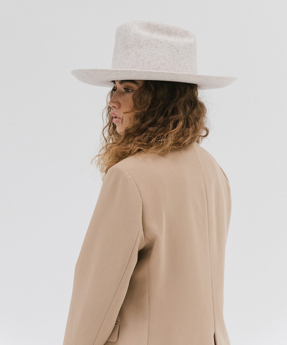 Woman wearing a mix grey colored Western hat with a classic cattleman crown, and a beige coat against a plain background  #color_mix grey