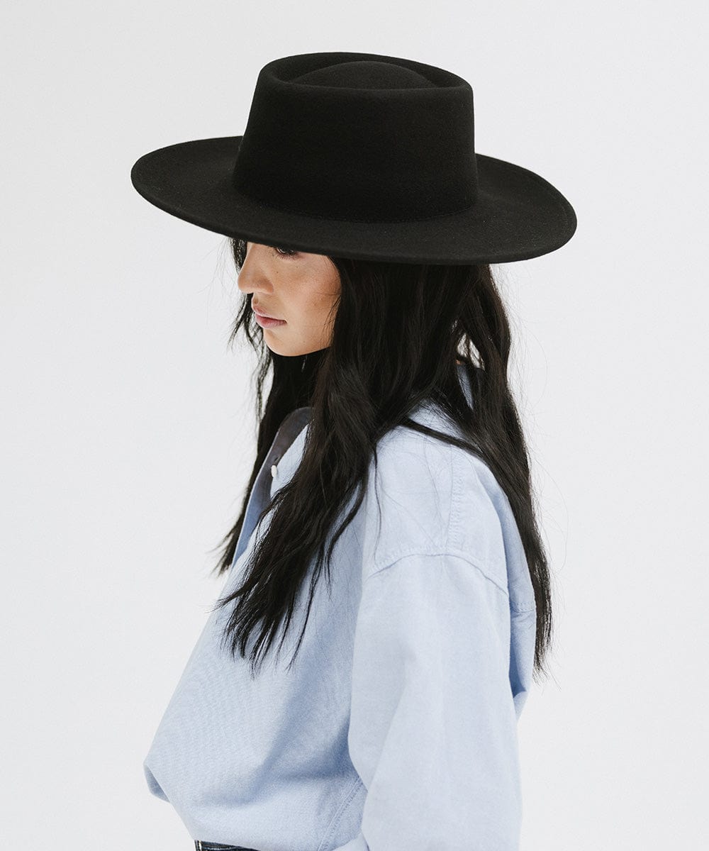 Woman wearing a black gambler hat and a blue shirt, facing sideways against a plain background #color_black
