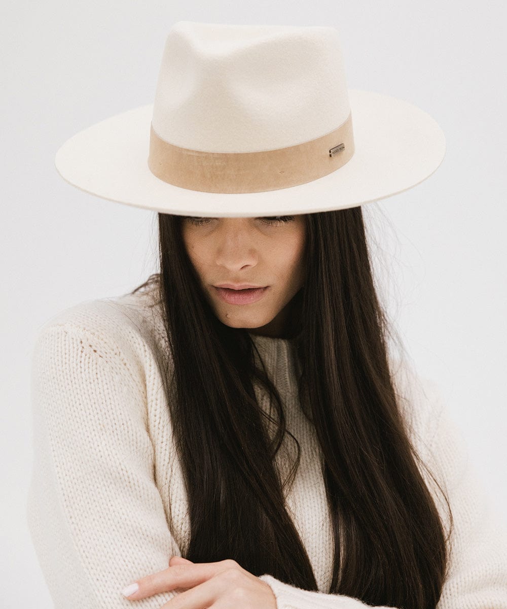 Woman wearing a off white felt fedora hat with a band and a white sweater, posing against a plain background  #color_off white