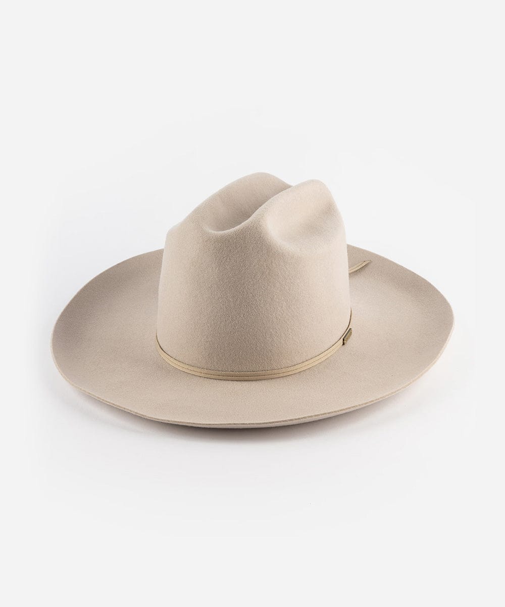 An ivory colored Western hat with a classic cattleman crown and an upturned brim. It features a tall crown and a stiff brim with a tonal grosgrain band and a brass Gigi Pip pin. #color_ivory