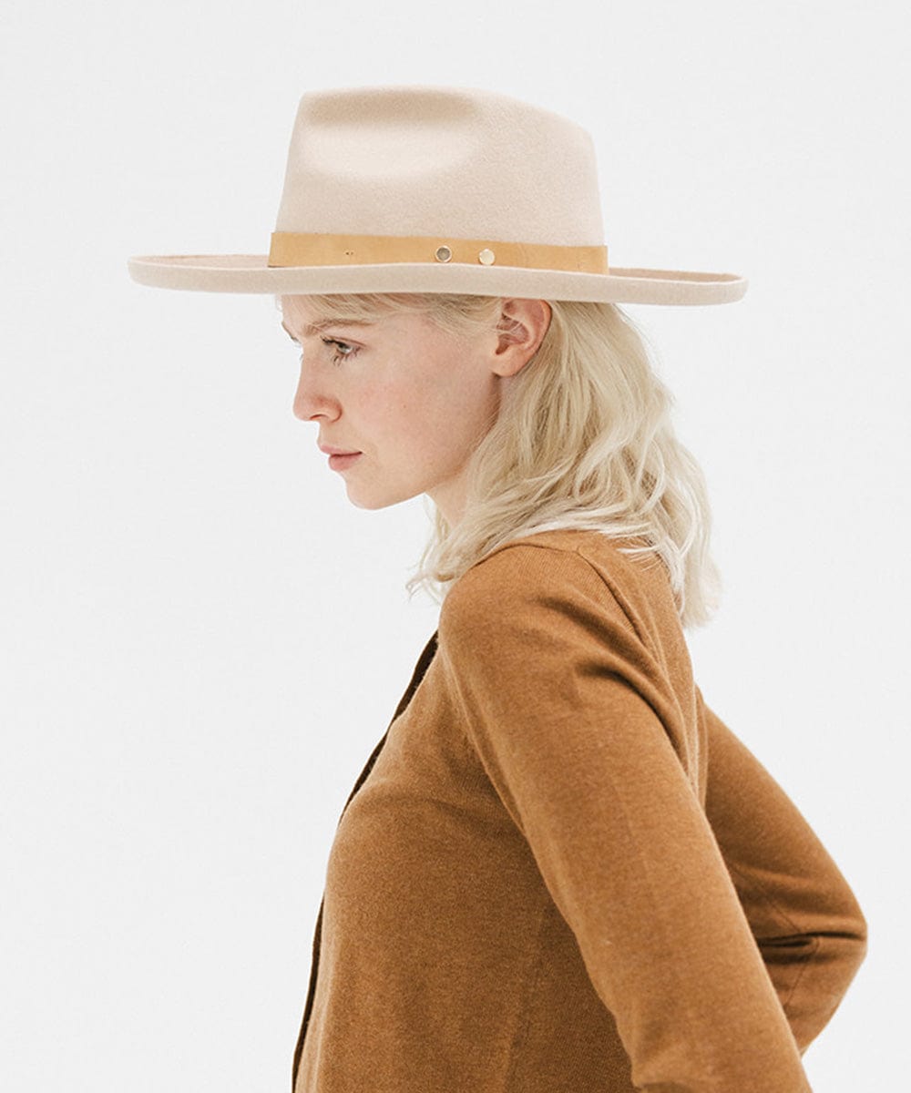 Woman wearing a cream felt fedora hat with a hat band and a brown sweater, facing sideways against a plain background  #color_cream