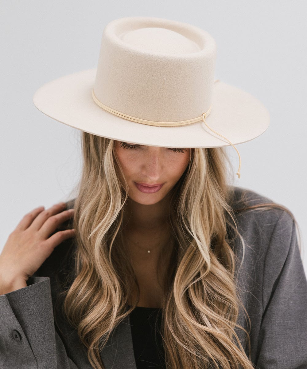 Woman wearing a cream Maise classic flat brim hat with a hat band and a grey blazer, posing against a plain background #color_cream