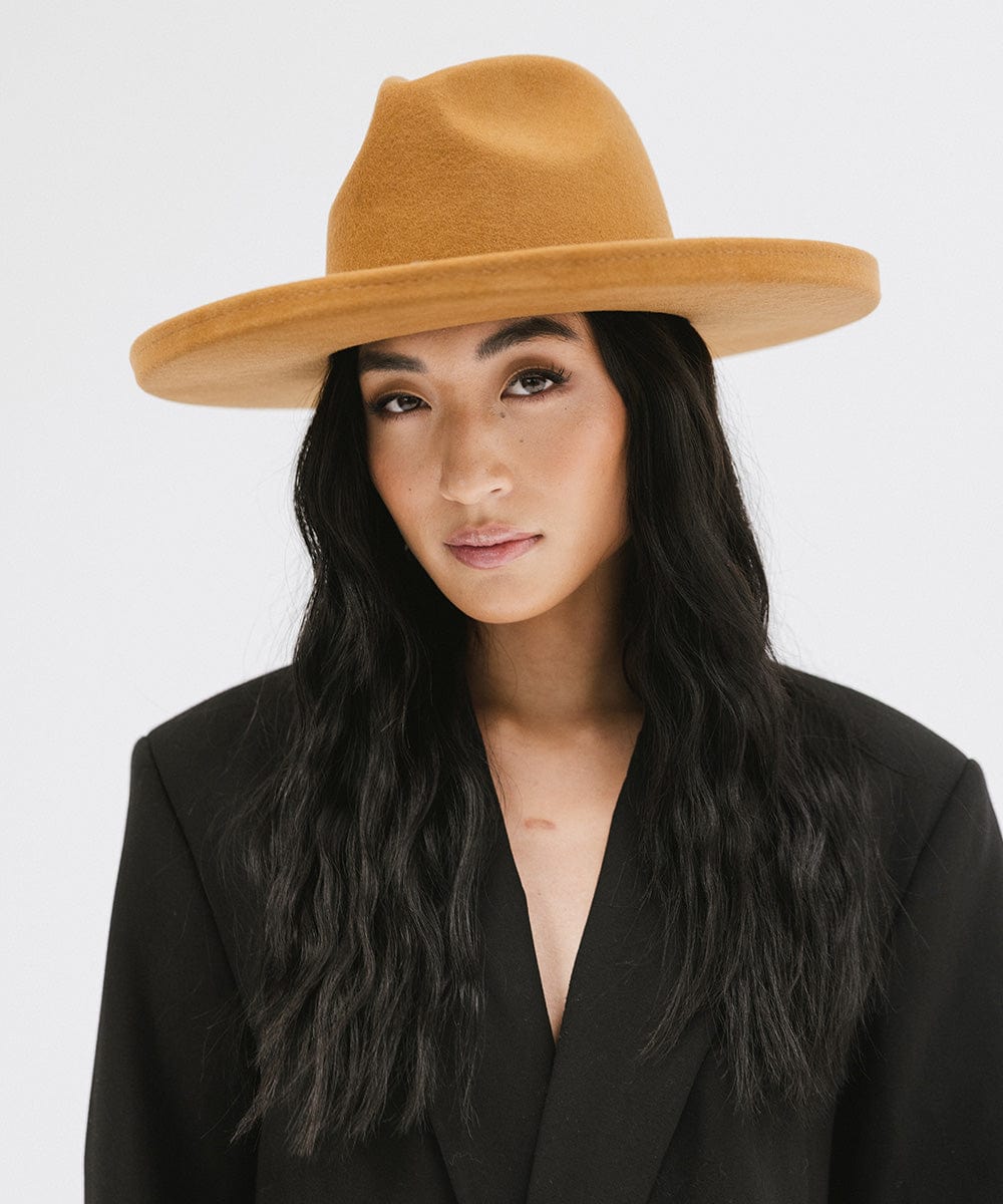 Woman wearing a cinnamon colored  wide brim felt fedora hat and a black blazer against a white background #color_cinnamon