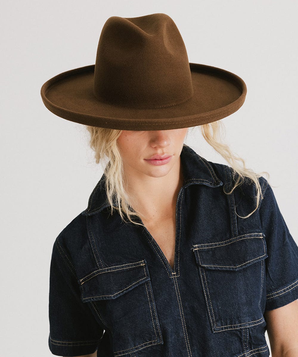Woman wearing a chocolate colored pencil brim fedora hat and a denim shirt, looking down against a plain background #color_chocolate