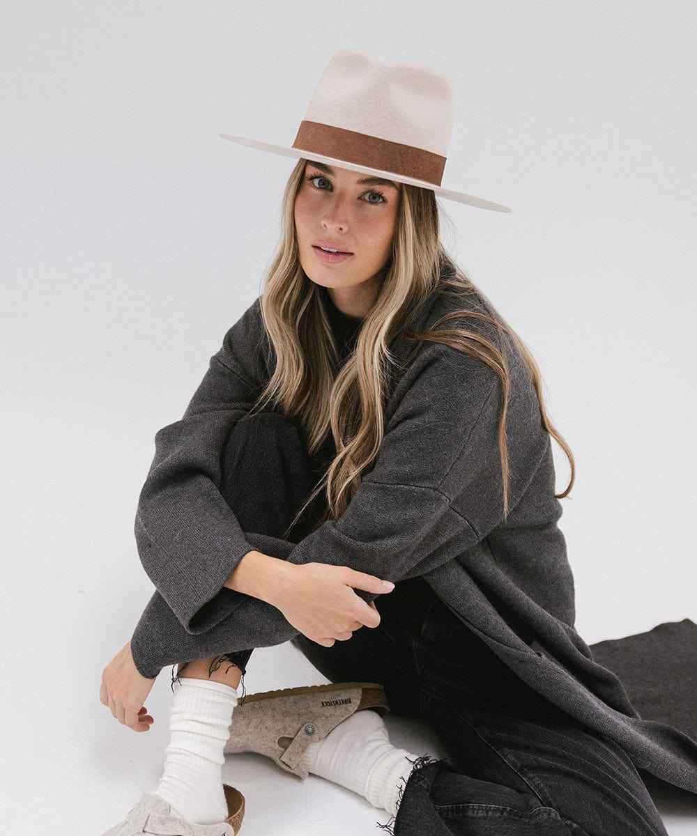 Woman wearing an ivory colored hat with a brown band and a dark coat on a white background #color_ivory
