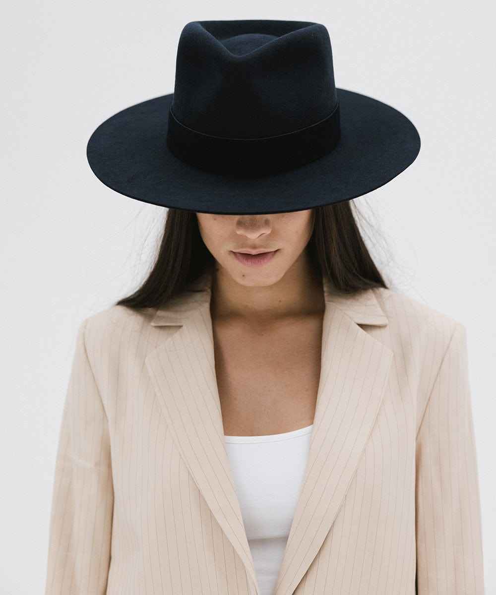Person wearing a navy fedora hat and beige blazer on a white background #color_navy