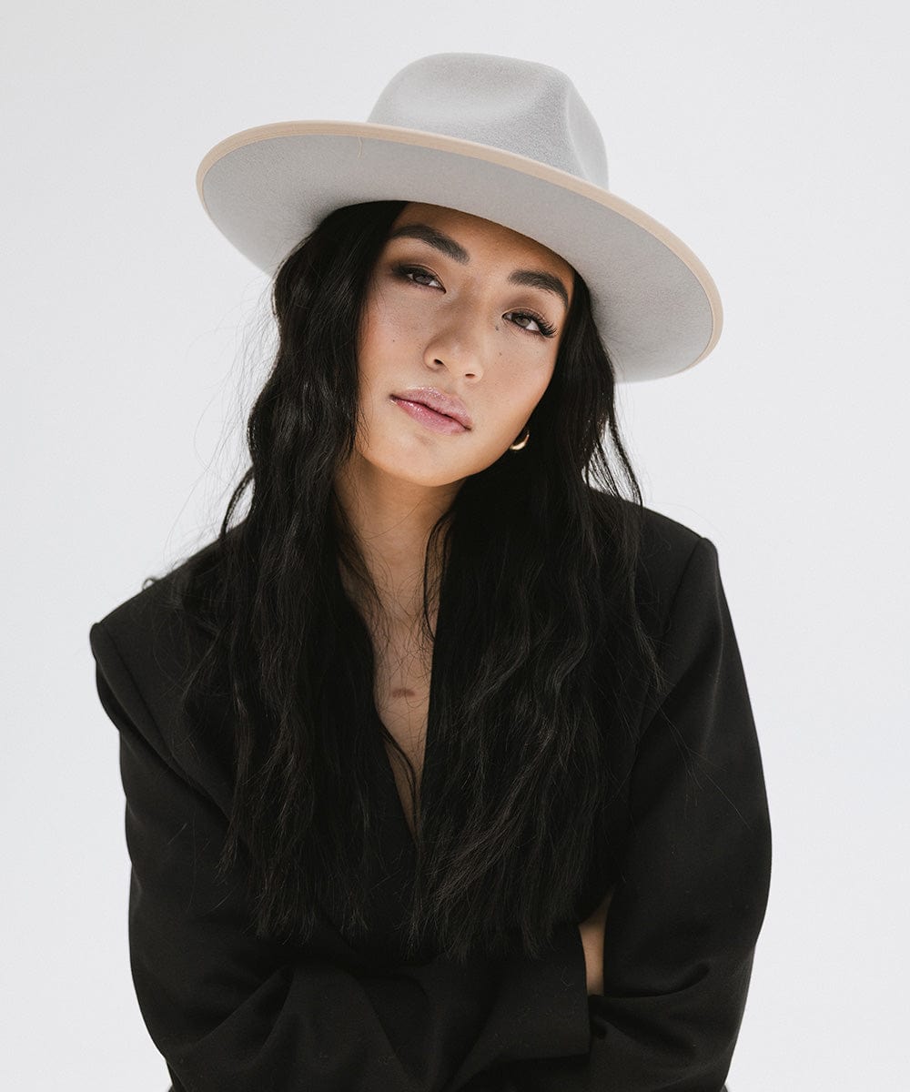 Woman wearing a light grey fedora hat and black blazer against a white background #color_light grey-tan