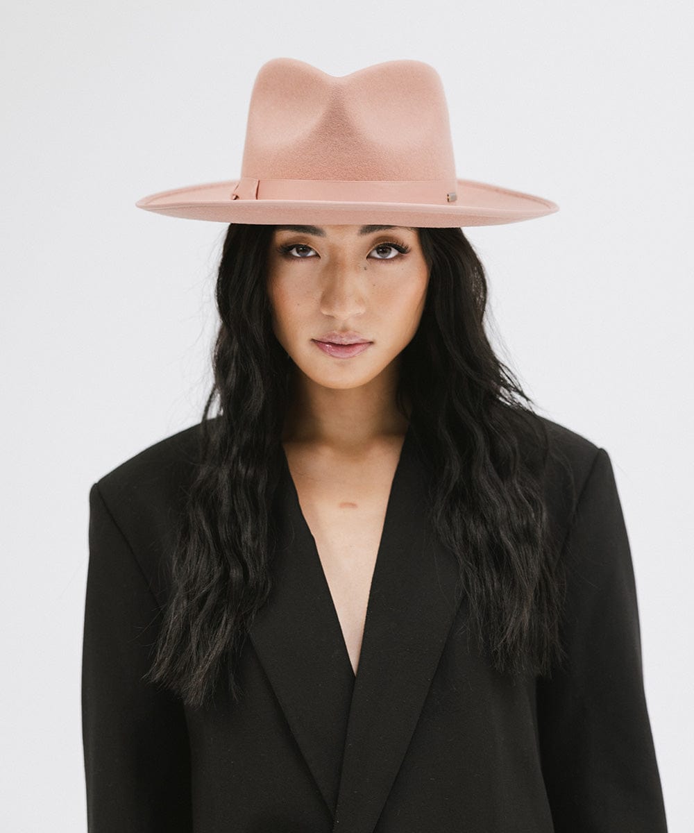 Woman wearing a pink fedora hat and black blazer against a white background #color_dusty pink
