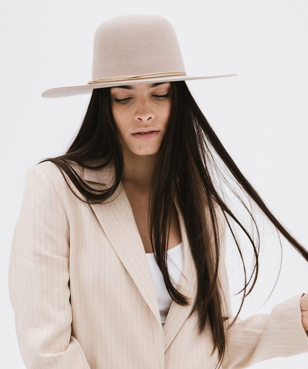Woman wearing a sand colored open crown hat with a hat band and a cream blazer, posing against a plain background #color_sand
