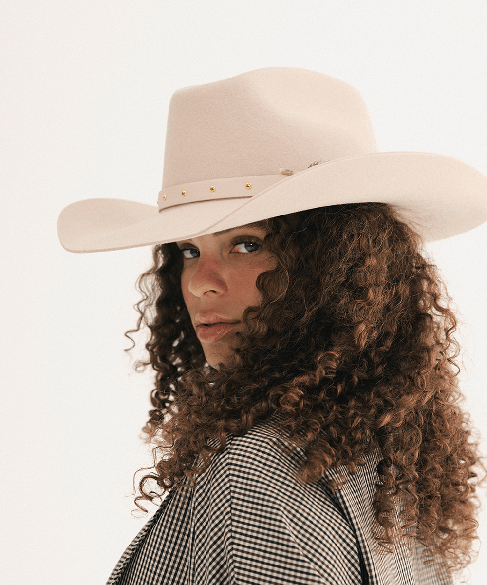 Woman wearing a cream cowboy hat with an upturned brim and an attached cream leather band, plaid shirt on a white background #color_cream