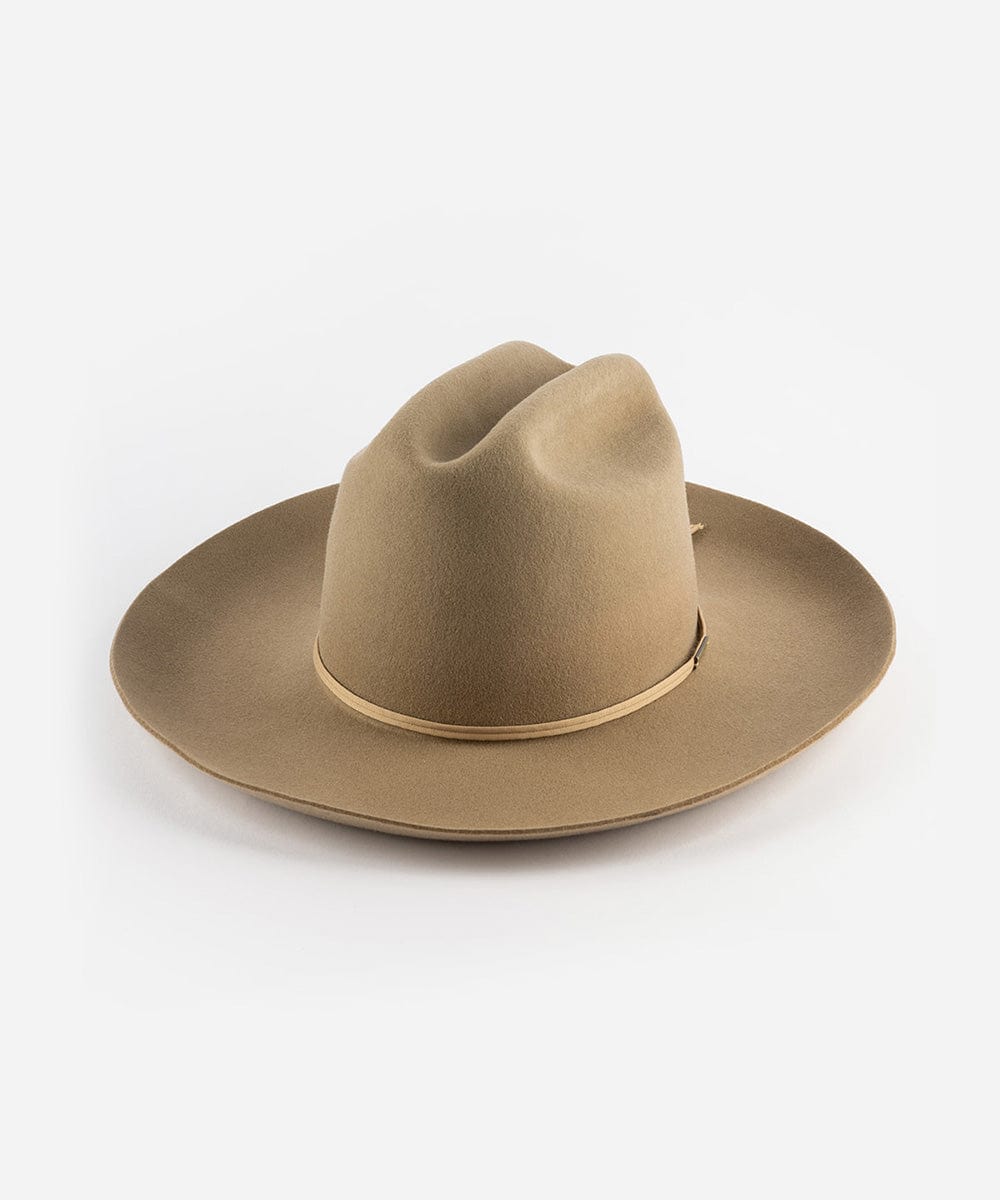 A tan Western hat with a classic cattleman crown and an upturned brim. It features a tall crown and a stiff brim with a tonal grosgrain band and a brass Gigi Pip pin. #color_tan