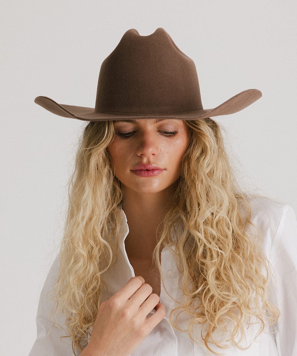 Woman wearing a chocolate colored cowboy hat and a white shirt against a plain background #color_chocolate