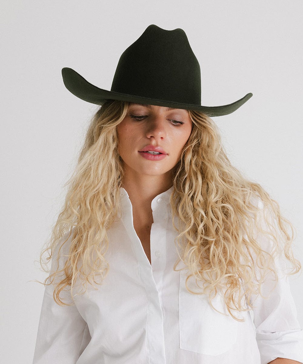Woman wearing a dark green cowboy hat against a plain background #color_dark green
