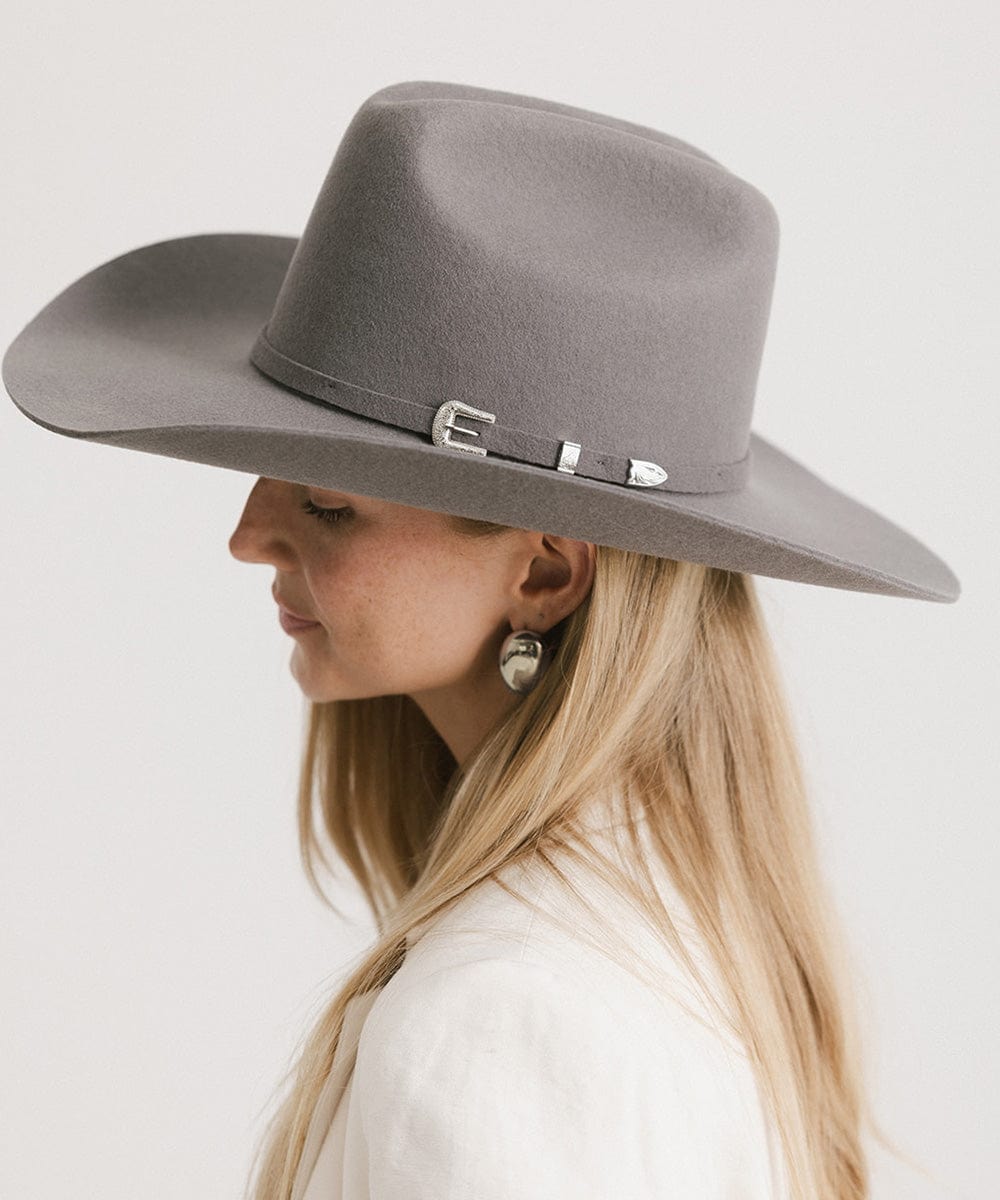 Woman wearing a limited edition stone colored cowboy hat with a hat band and a white blazer, facing sideways against a plain background #color_limited edition stone