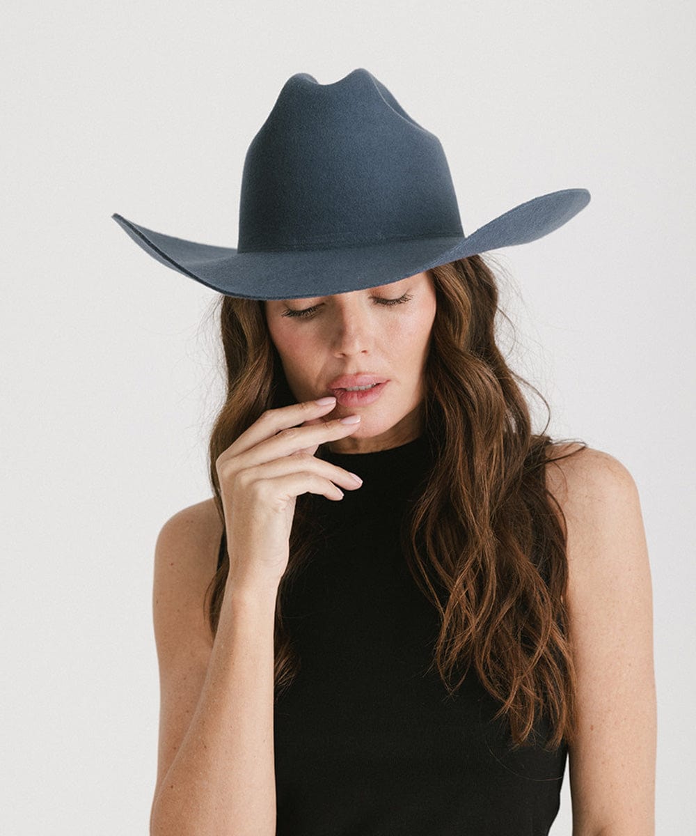 Woman wearing a vintage blue colored cowboy hat and a black top against a plain background #color_vintage blue