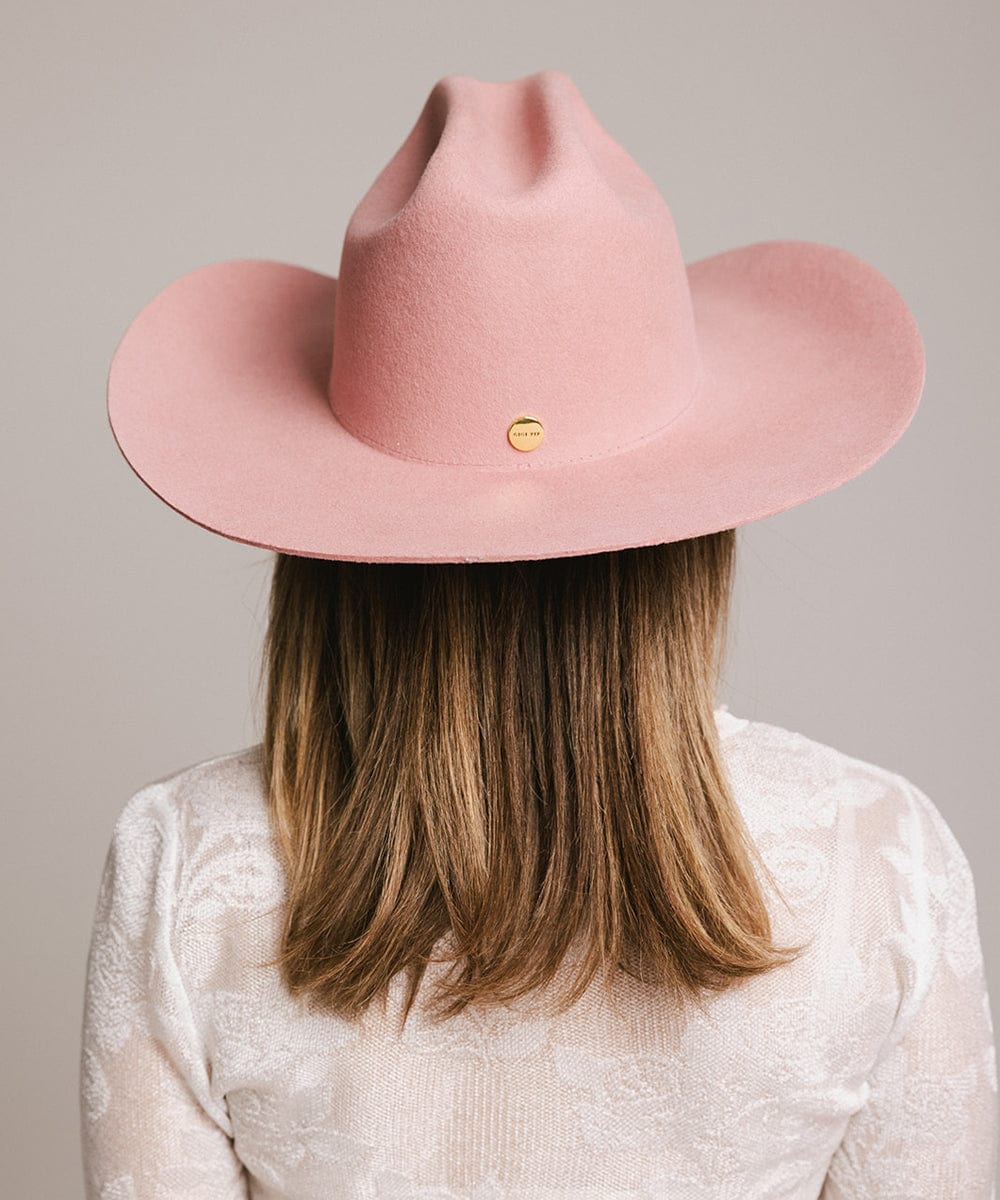 Woman wearing a rose colored cowboy hat and a white t-shirt, facing behind against a plain background #color_rose