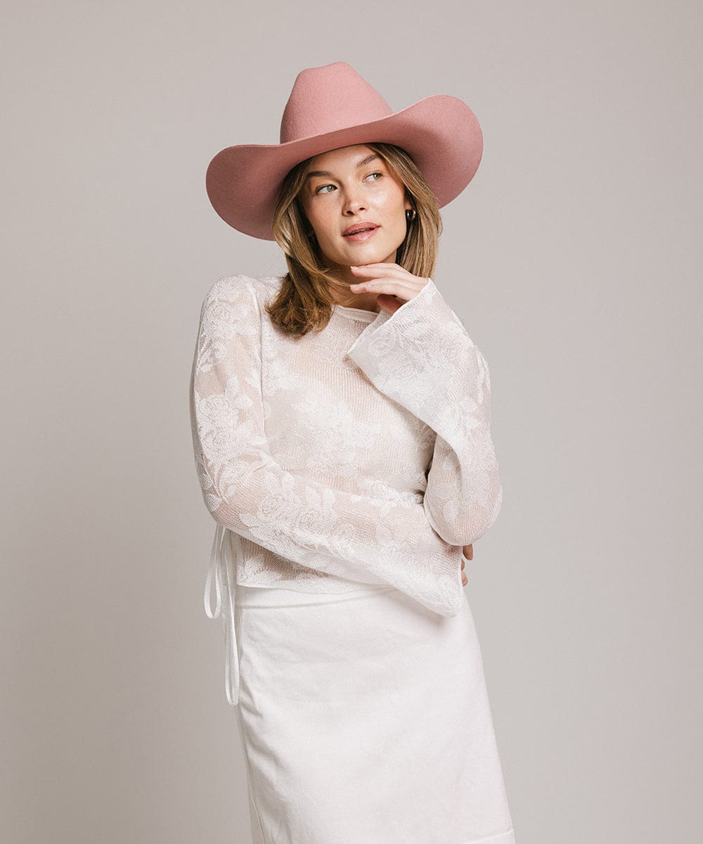 Woman wearing a rose colored cowboy hat, a white t-shirt and white skirt against a plain background #color_rose