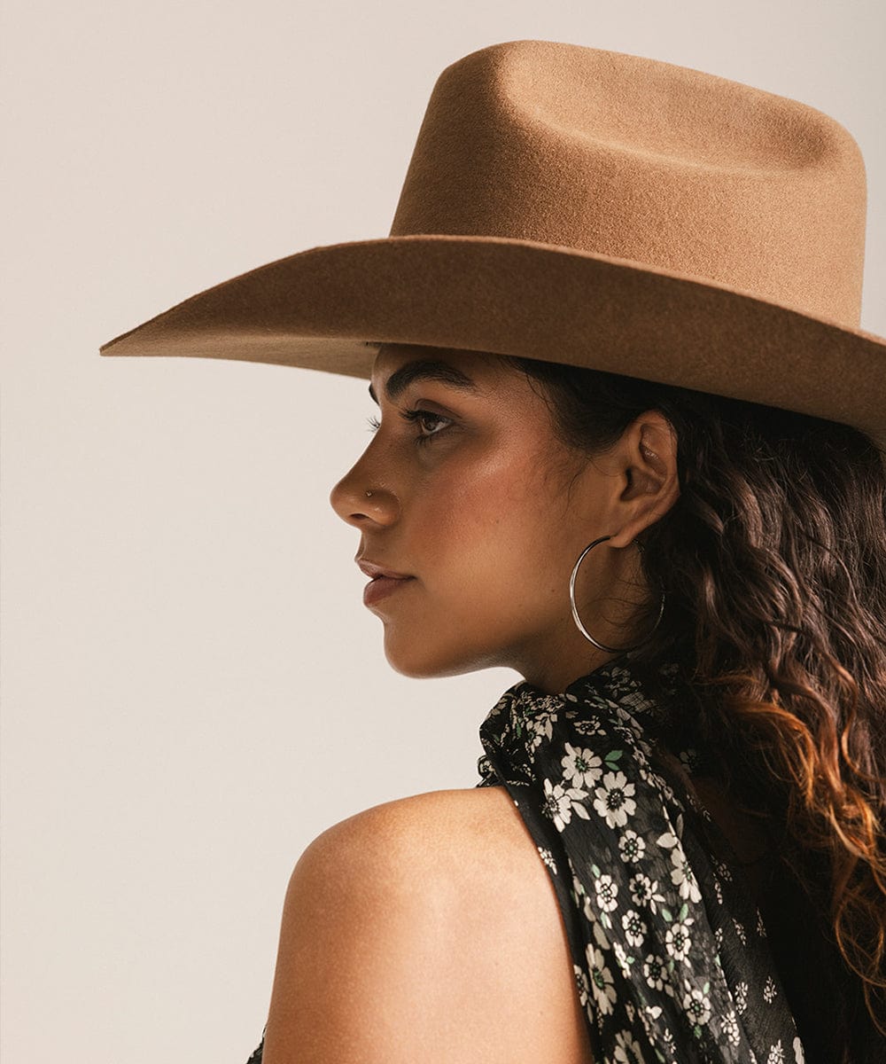Woman wearing a caramel colored cowboy hat and a black floral halter top, facing sideways against a plain background #color_caramel