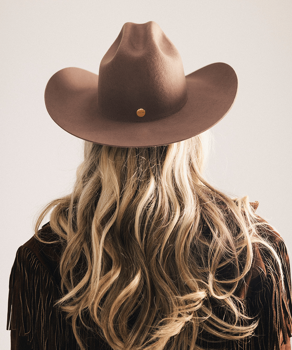 Woman wearing a brown cowboy hat and fringed jacket on a plain background #color_chocolate