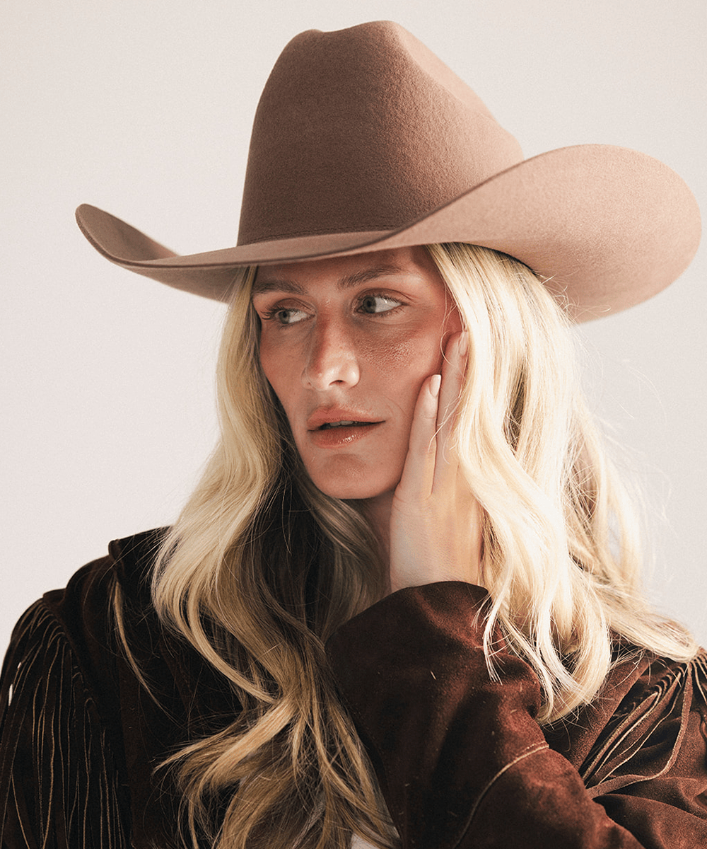 Woman wearing a brown cowboy hat and fringed jacket on a plain background #color_chocolate