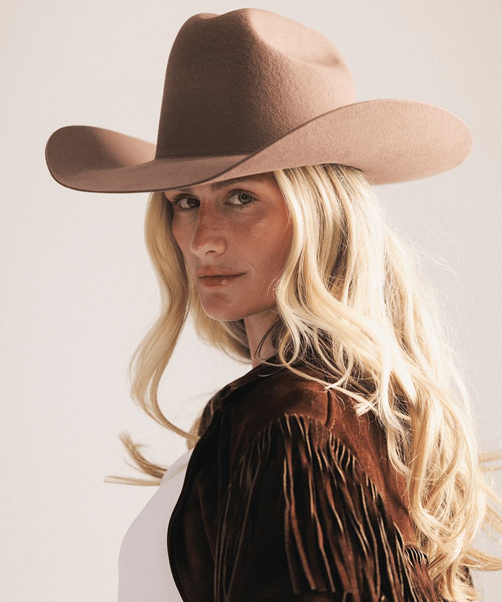 Woman wearing a brown cowboy hat and fringed jacket on a plain background #color_chocolate