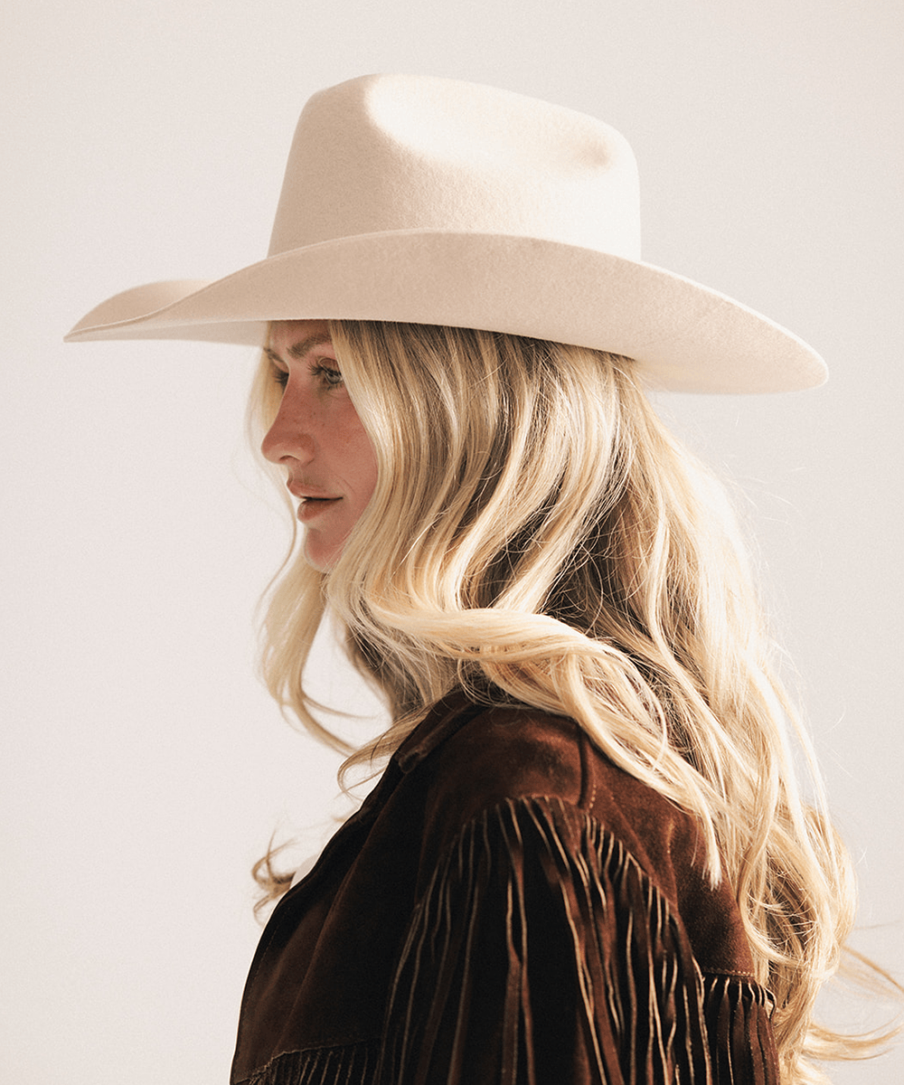 Woman wearing a beige cowboy hat and brown jacket on a light background #color_cream