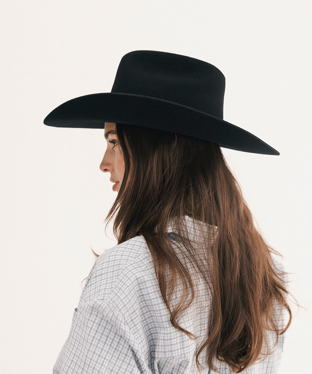 A woman in profile wearing a black wide-brim fedora hat and a light blue and white checkered shirt, photographed against a clean white background #color_black