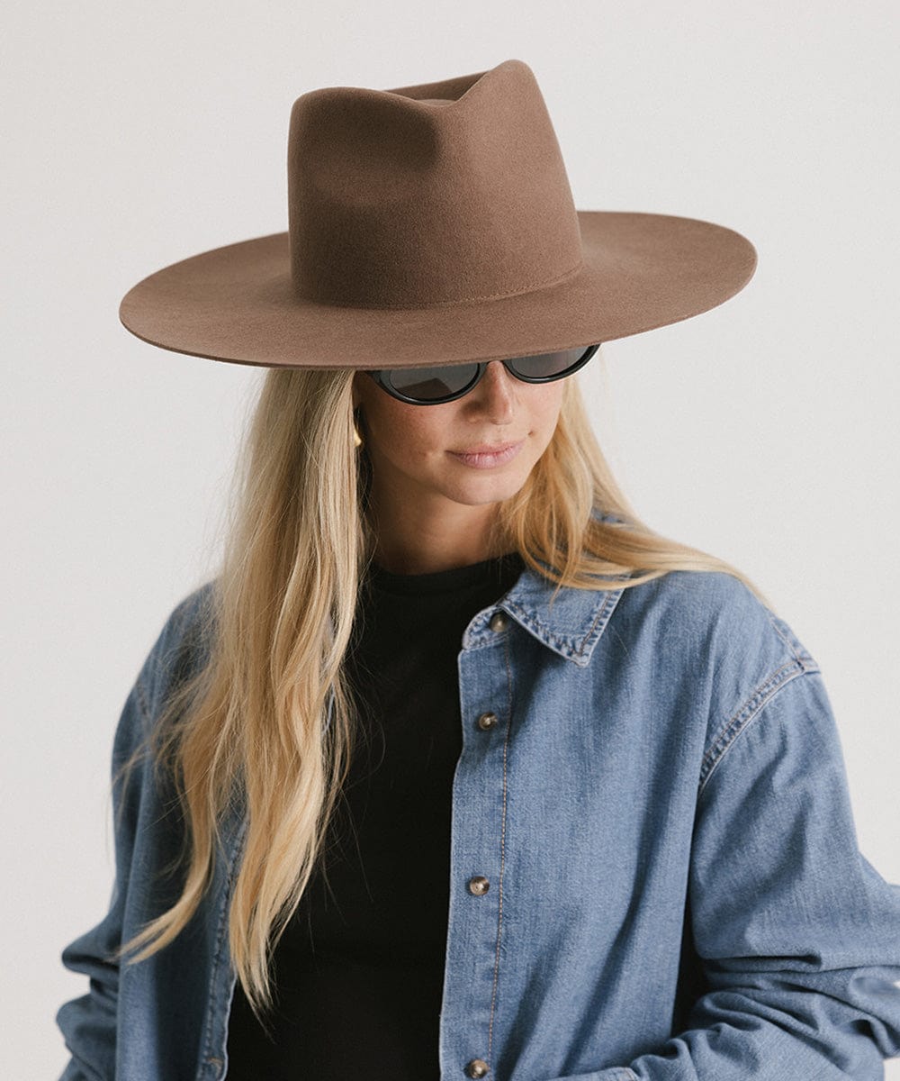 Woman wearing a chocolate colored Wesley Wide Brim Fedora Hat, sunglasses and a denim shirt against a plain background #color_chocolate