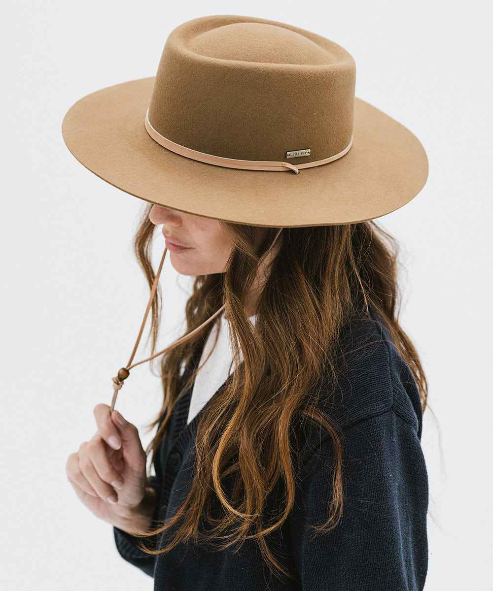 Woman wearing a brown hat with a hat band and a dark blue sweater, posing sideways against a white background #color_brown