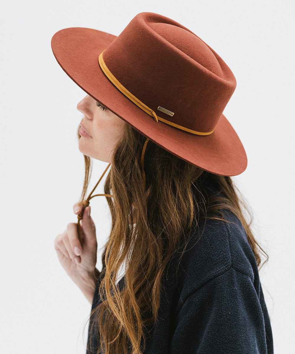 Woman wearing a rusty red colored fedora hat with a gold band on a white background #color_rusty red