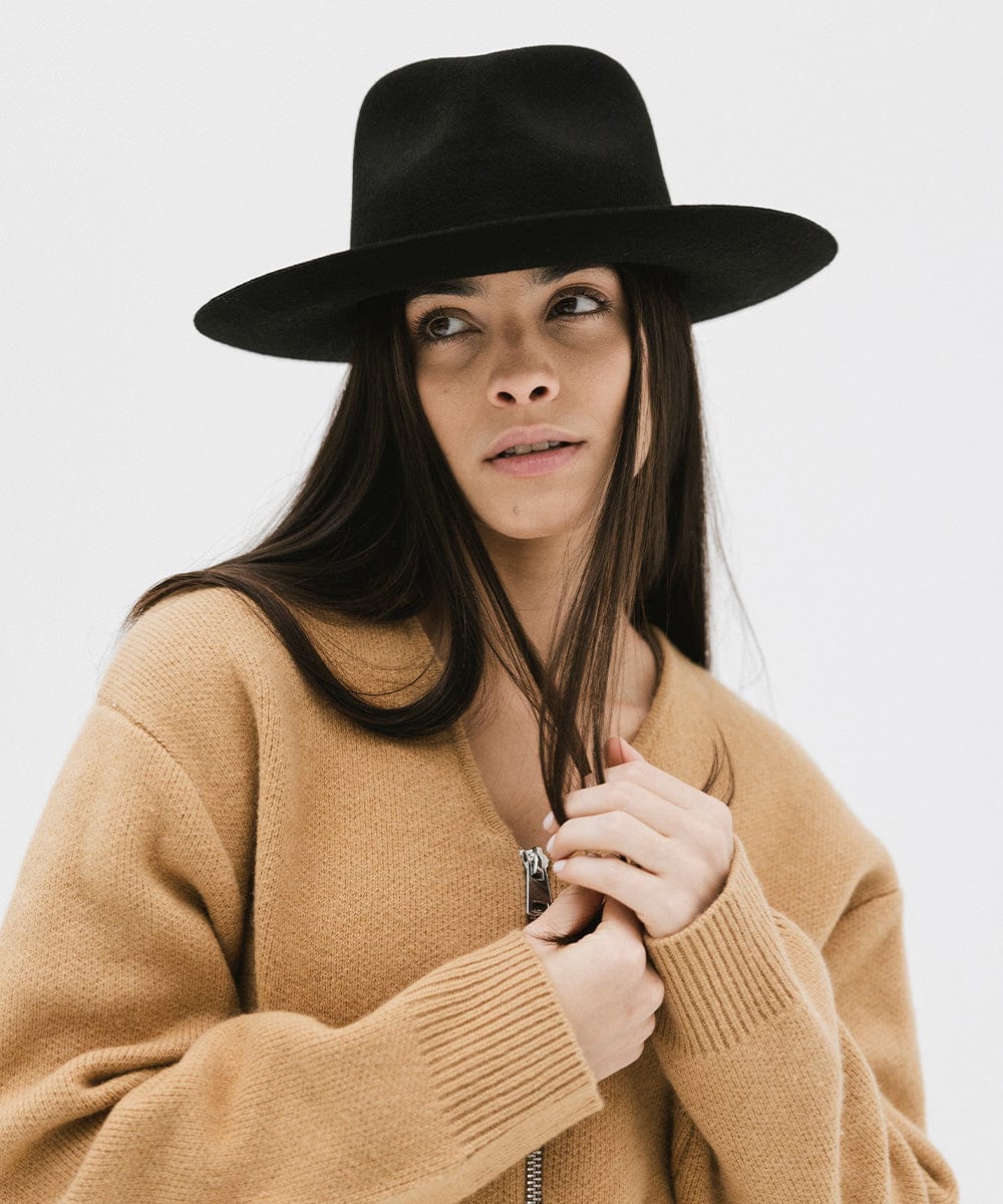 Woman wearing a black fedora hat and a brown jacket against a white background #color_black