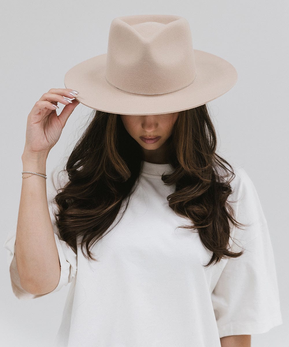 Woman wearing a cream fedora hat and a white shirt, looking down against a white background #color_cream