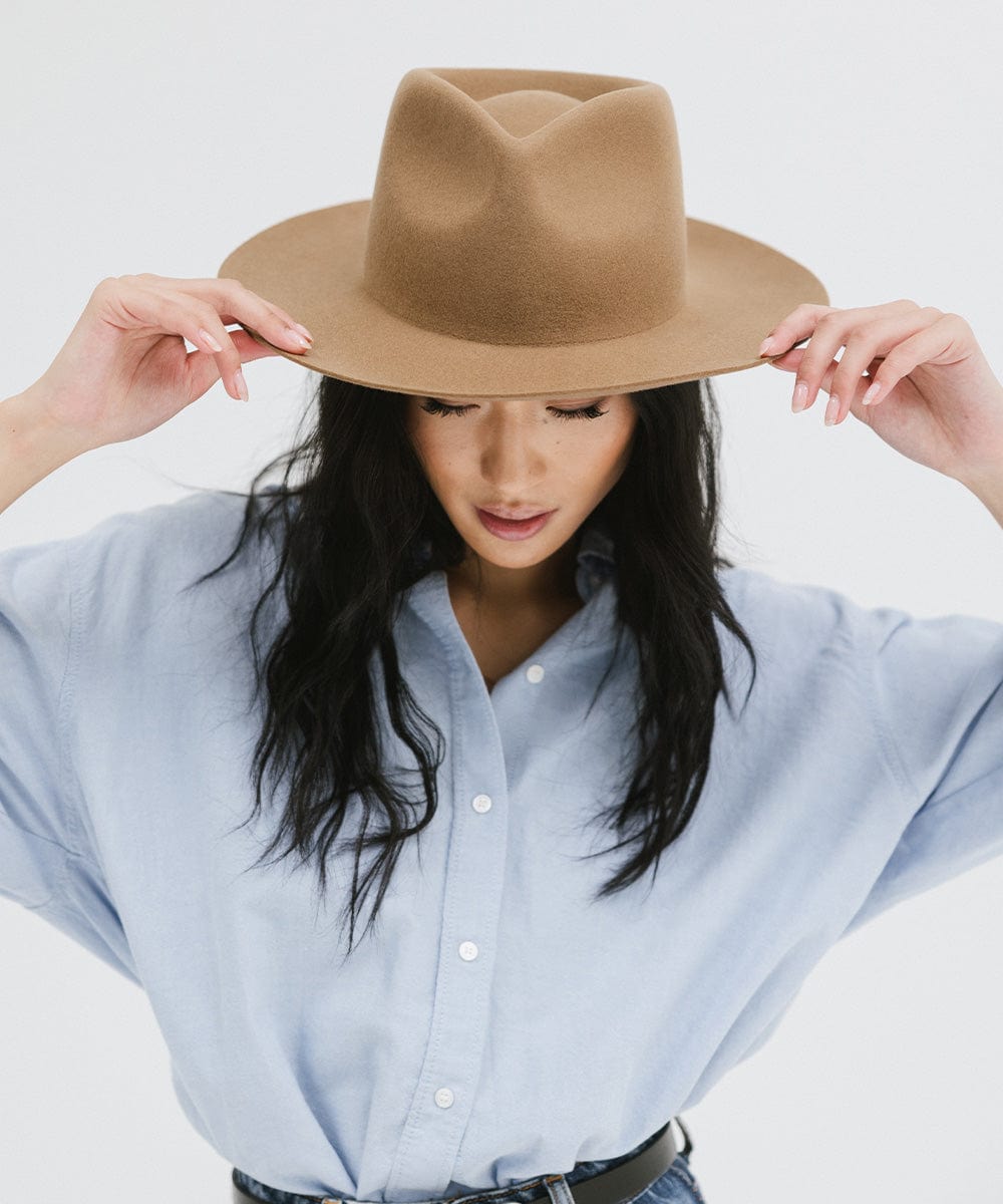 Woman wearing a brown fedora hat and a light blue shirt against a white background #color_brown