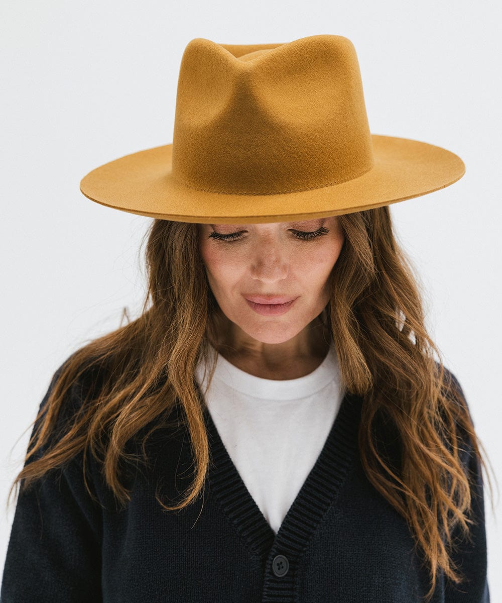 Woman wearing a cinnamon colored fedora hat and a dark blue shirt against a white background #color_cinnamon