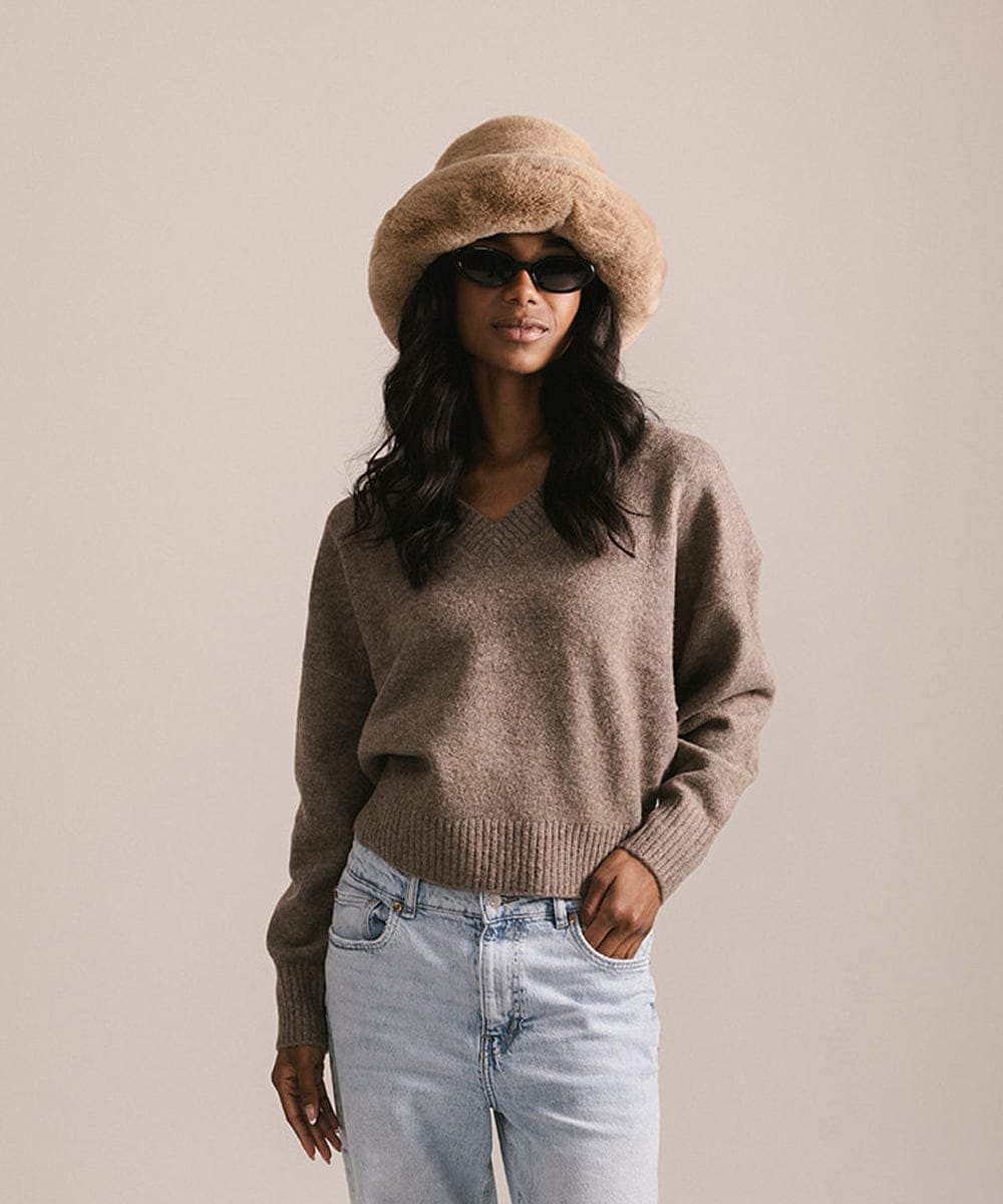 Woman wearing a brown sweater, light blue jeans, and a beige hat against a plain background #color_tan