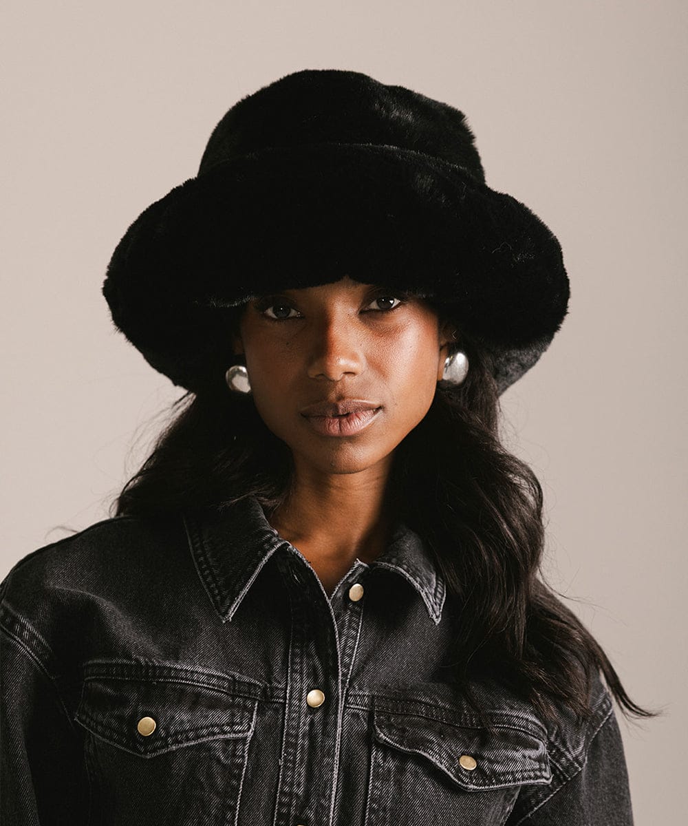 Woman wearing a black fur hat and denim jacket against a neutral background #color_black