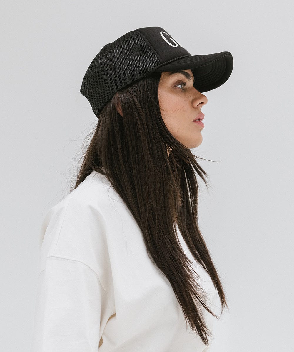 Woman wearing a black cap and a white t-shirt, facing sideways against a plain background #color_black