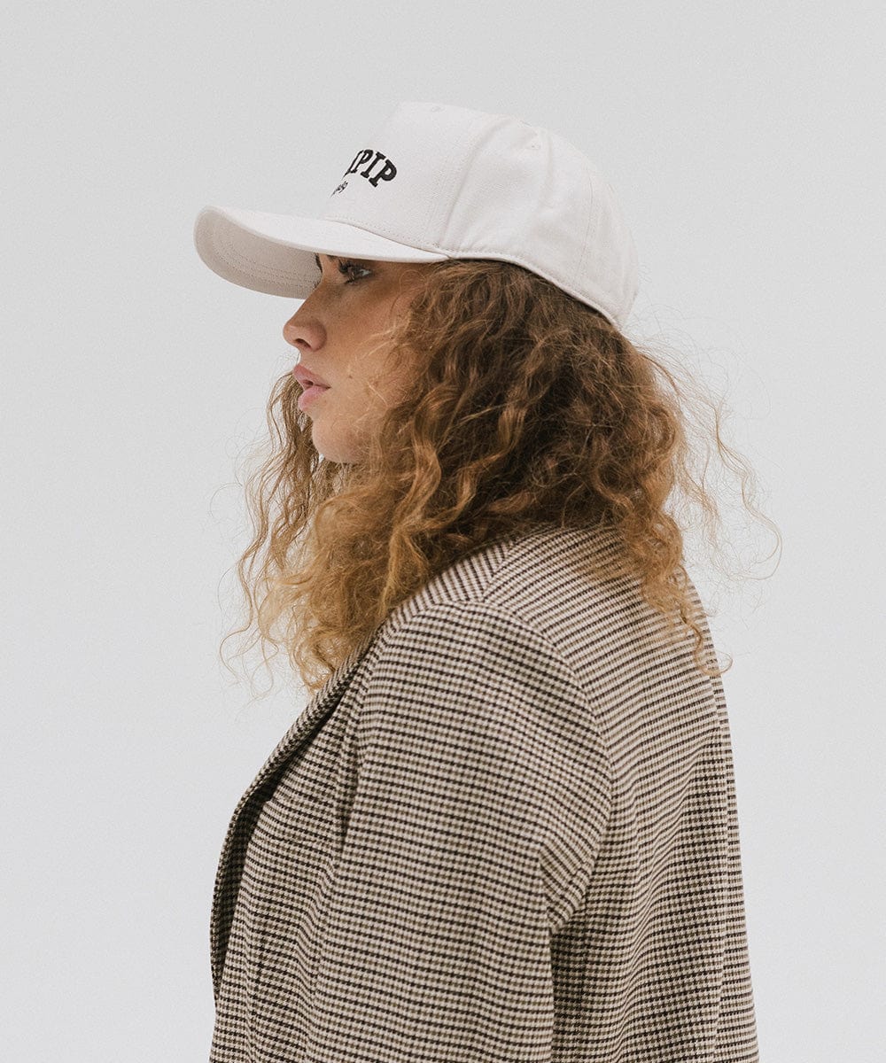 Woman wearing a cream trucker hat and a coat, facing sideways against a plain background #color_cream