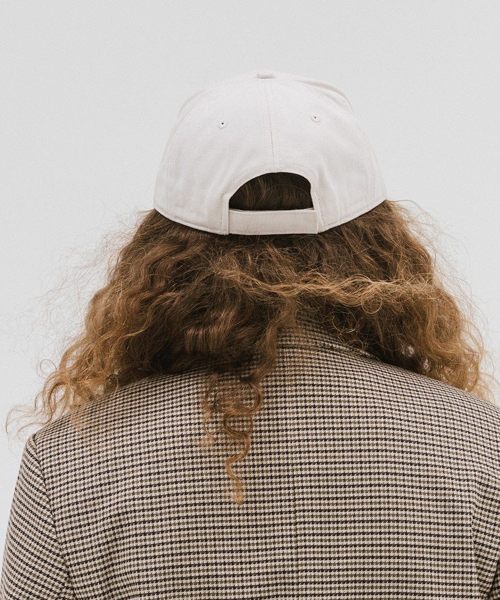 Woman wearing a cream trucker hat a coat against a plain background #color_cream